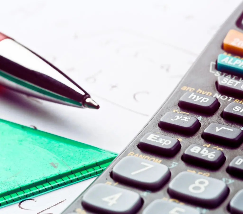 Obrazek wyróżniający w artykule - ile pracodawca dostaje za pracownika z grupą inwalidzką. Obraz przedstawia zbliżenie na kalkulator, długopis i zieloną teczkę. Kalkulator zajmuje większą część prawej strony zdjęcia, a na jego widocznych przyciskach można zobaczyć oznaczenia związane z funkcjami matematycznymi. Obok niego, po lewej stronie, leży metalowy długopis. Tło stanowi papier z odręcznymi notatkami lub obliczeniami. Scena sugeruje pracę związaną z obliczeniami lub analizą.