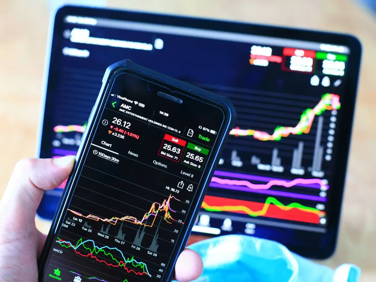 Zbliżenie na ekran smartfona z aplikacją giełdową pokazującą notowania akcji spółki AMC, z widocznym spadkiem ceny. W tle ekran tabletu z wykresami giełdowymi i danymi rynkowymi. Obraz symbolizuje emocje i dynamiczne zmiany towarzyszące debiutom giełdowym (IPO) oraz potrzebę świadomego podejmowania decyzji inwestycyjnych w obliczu zmienności rynku.